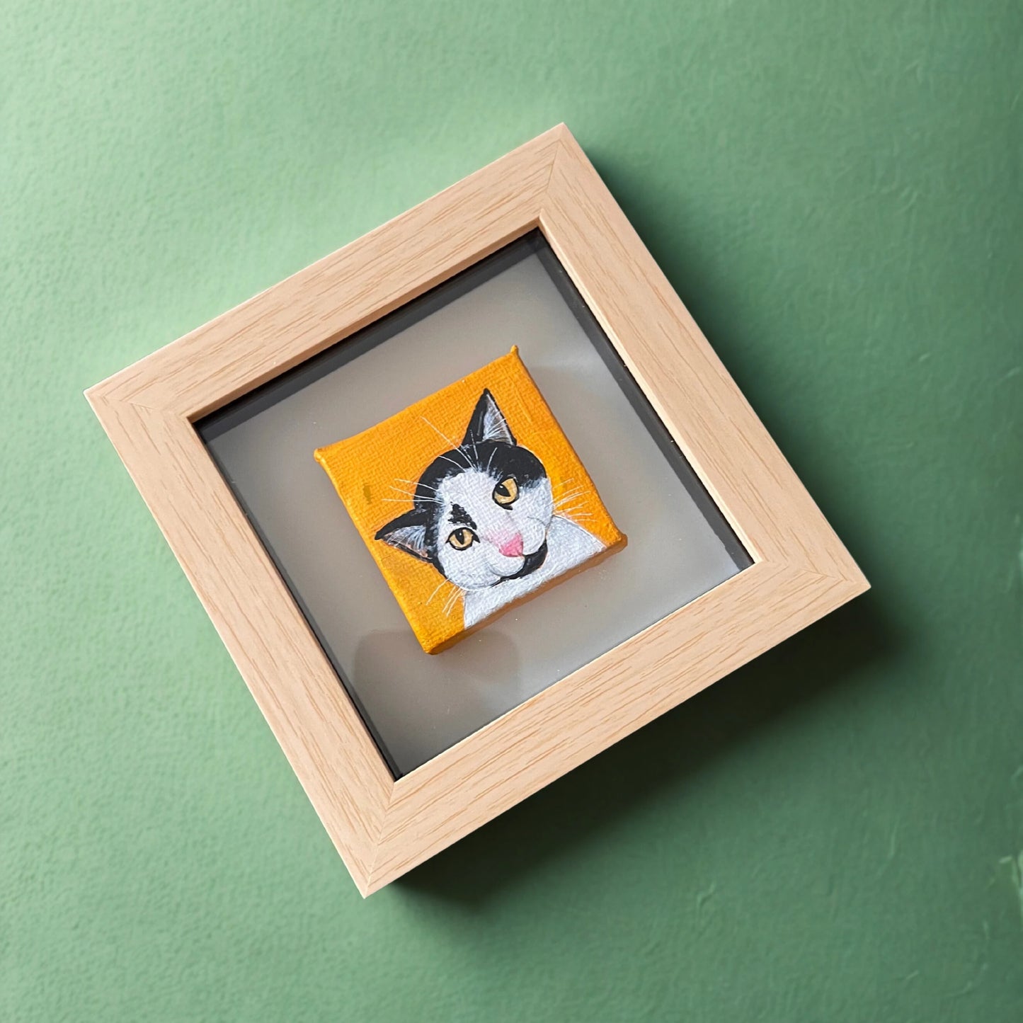 Framed artwork of a cat's face on an orange background against a green wall