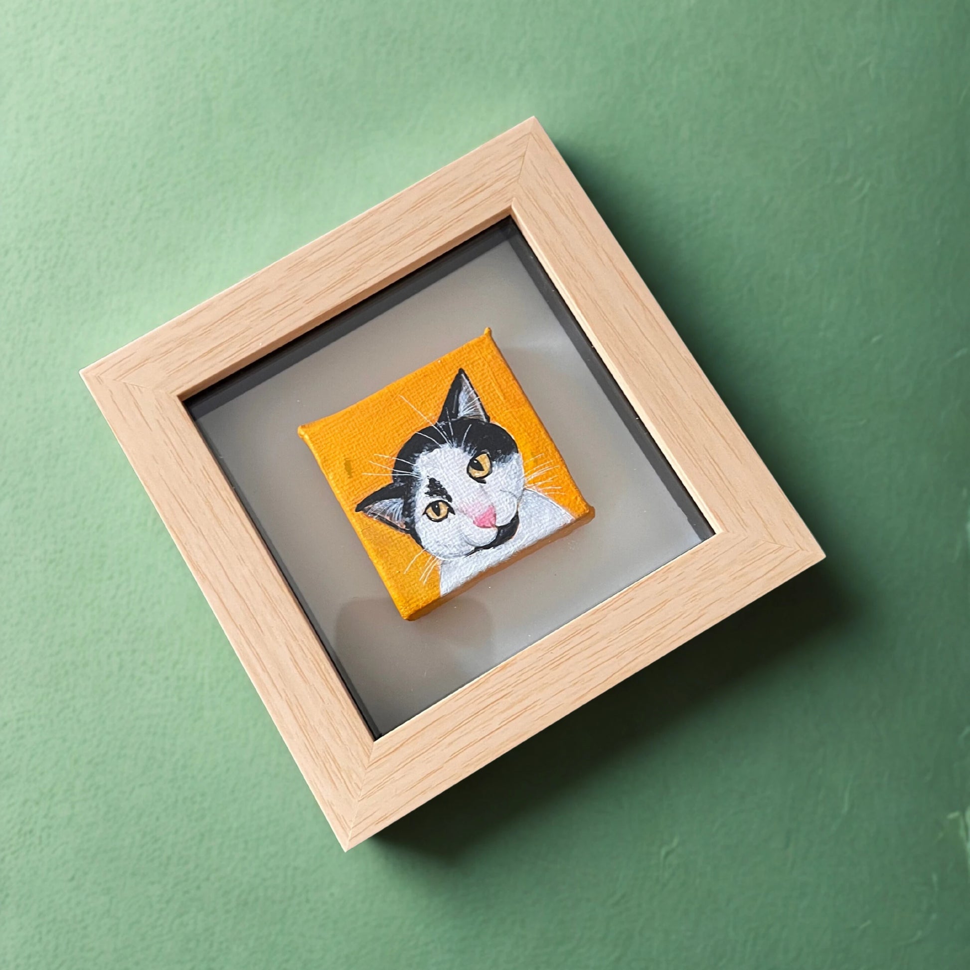 Framed artwork of a cat's face on an orange background against a green wall