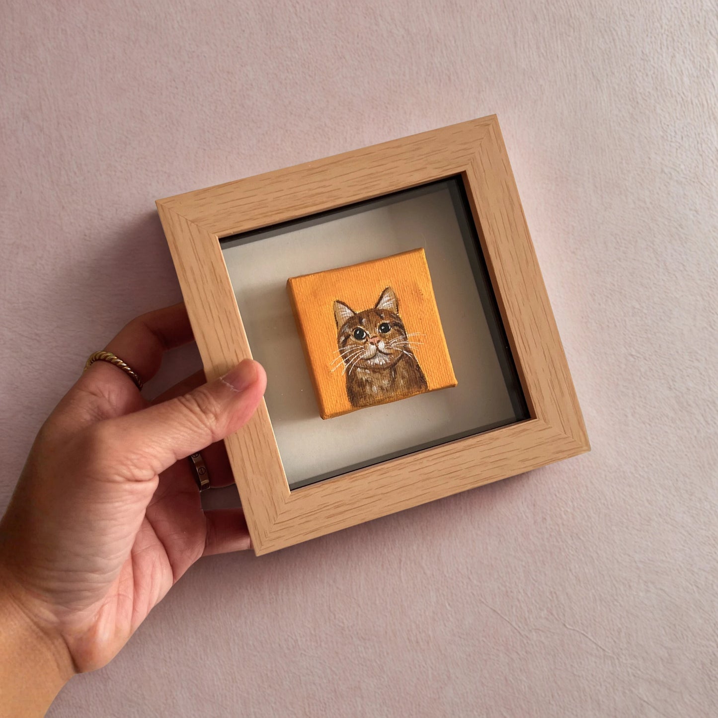 Hand holding a small wooden frame with a cat portrait on an orange background