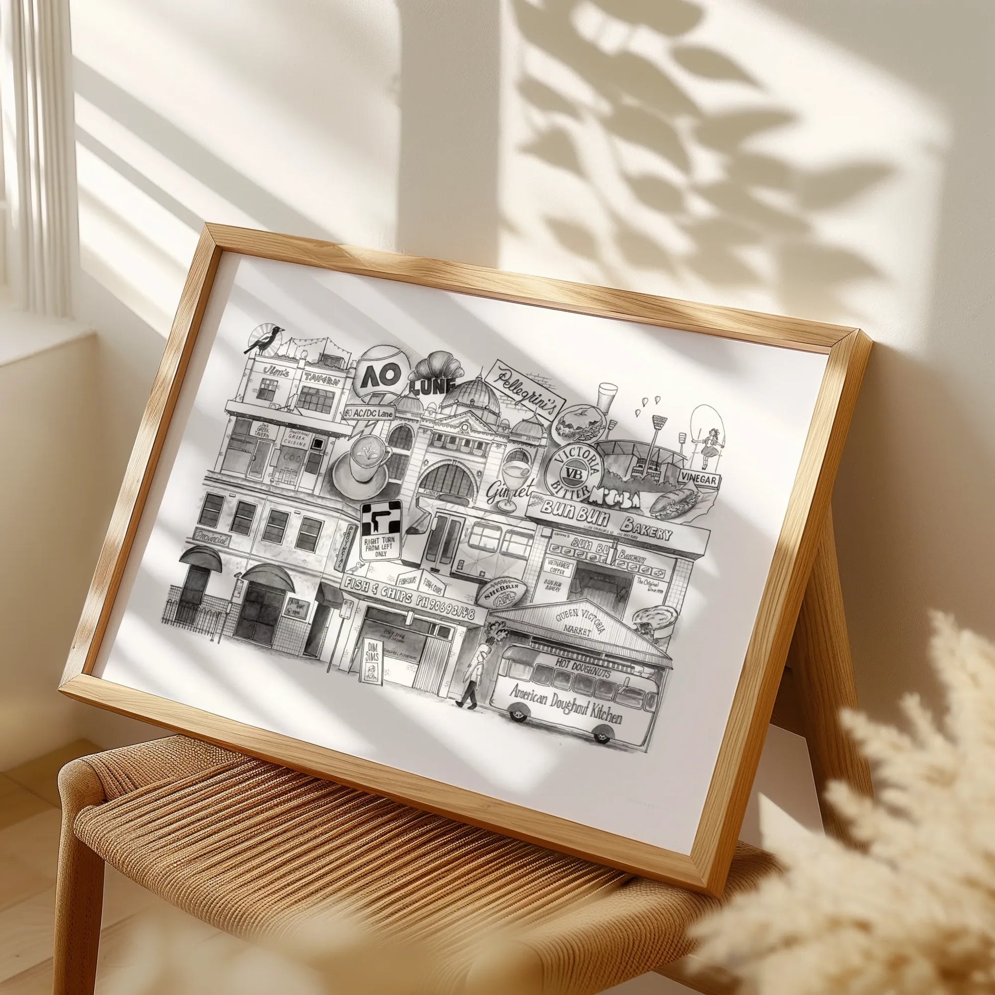 Framed black and white illustration of a city street scene on a white background, placed on a wooden stool.